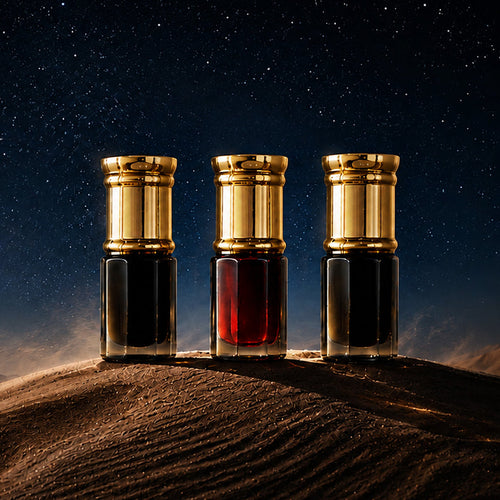 Three perfume bottles with gold caps stand on a desert sand dune under a starry night sky. The bottles contain dark and red liquids, with dramatic lighting highlighting their metallic caps and glass bodies.